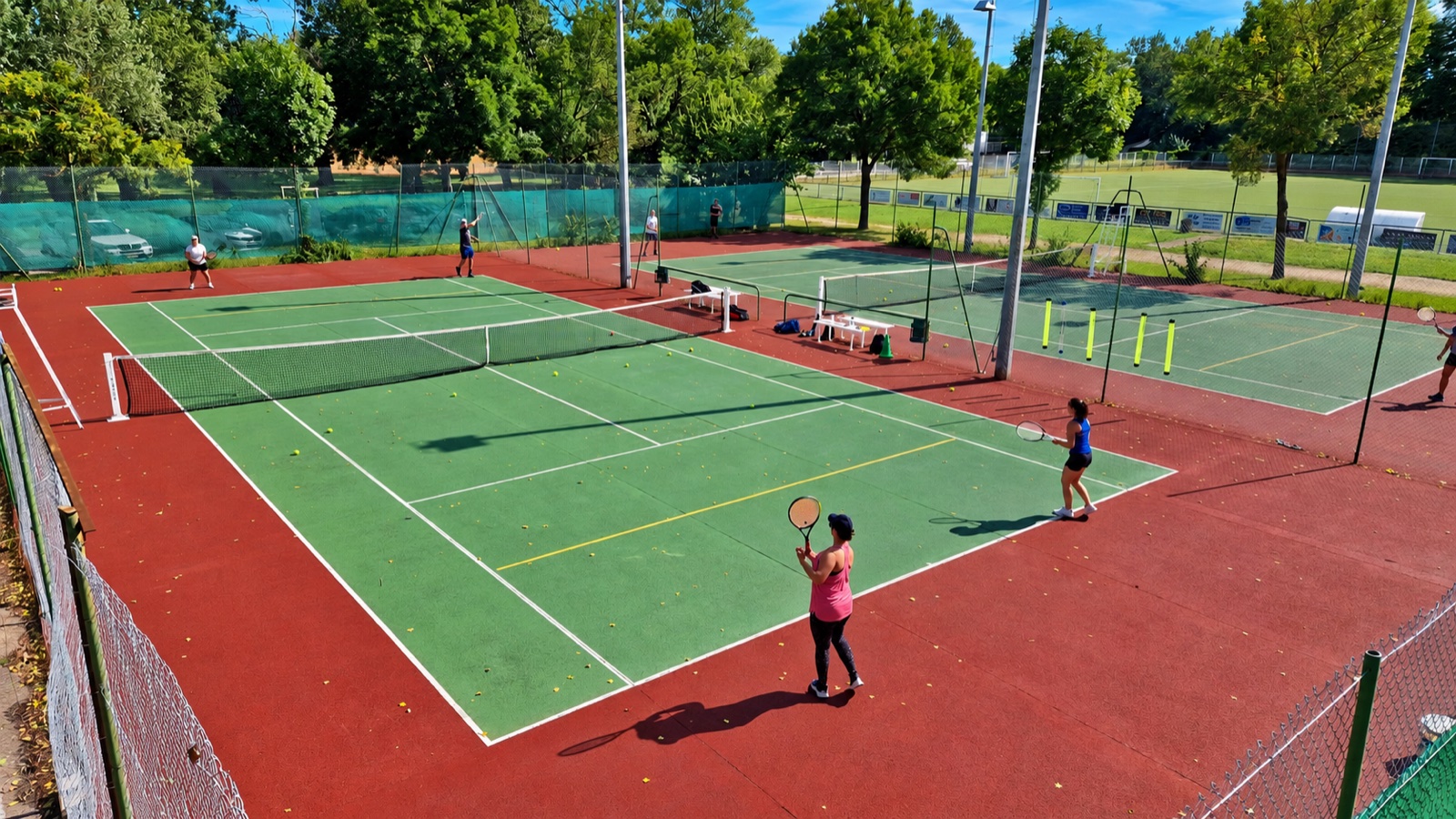 Des joueurs s’entraînent sur les deux courts du club, entourés d’arbres