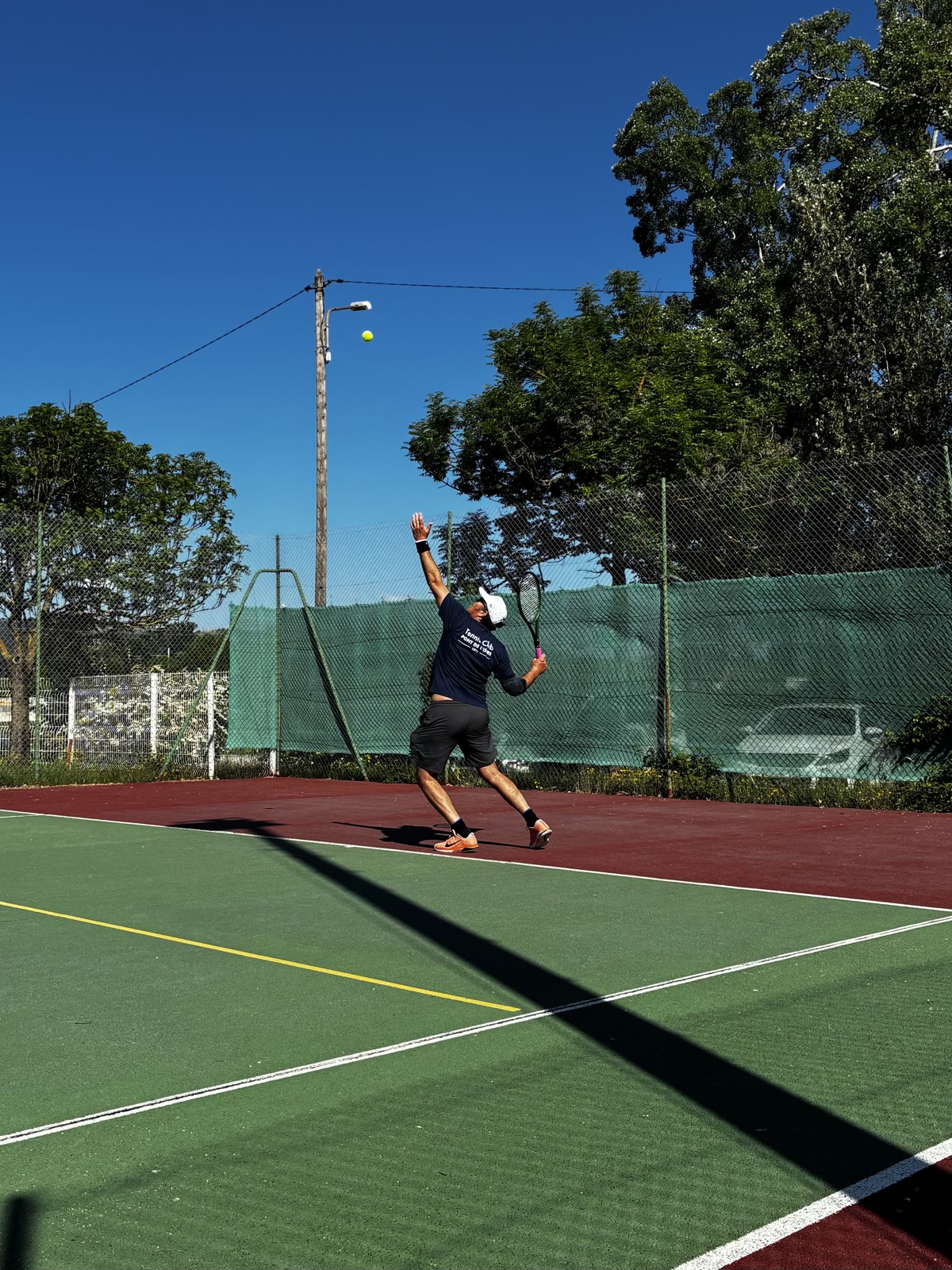 Un joueur au service sur un court du club, sous un ciel bleu